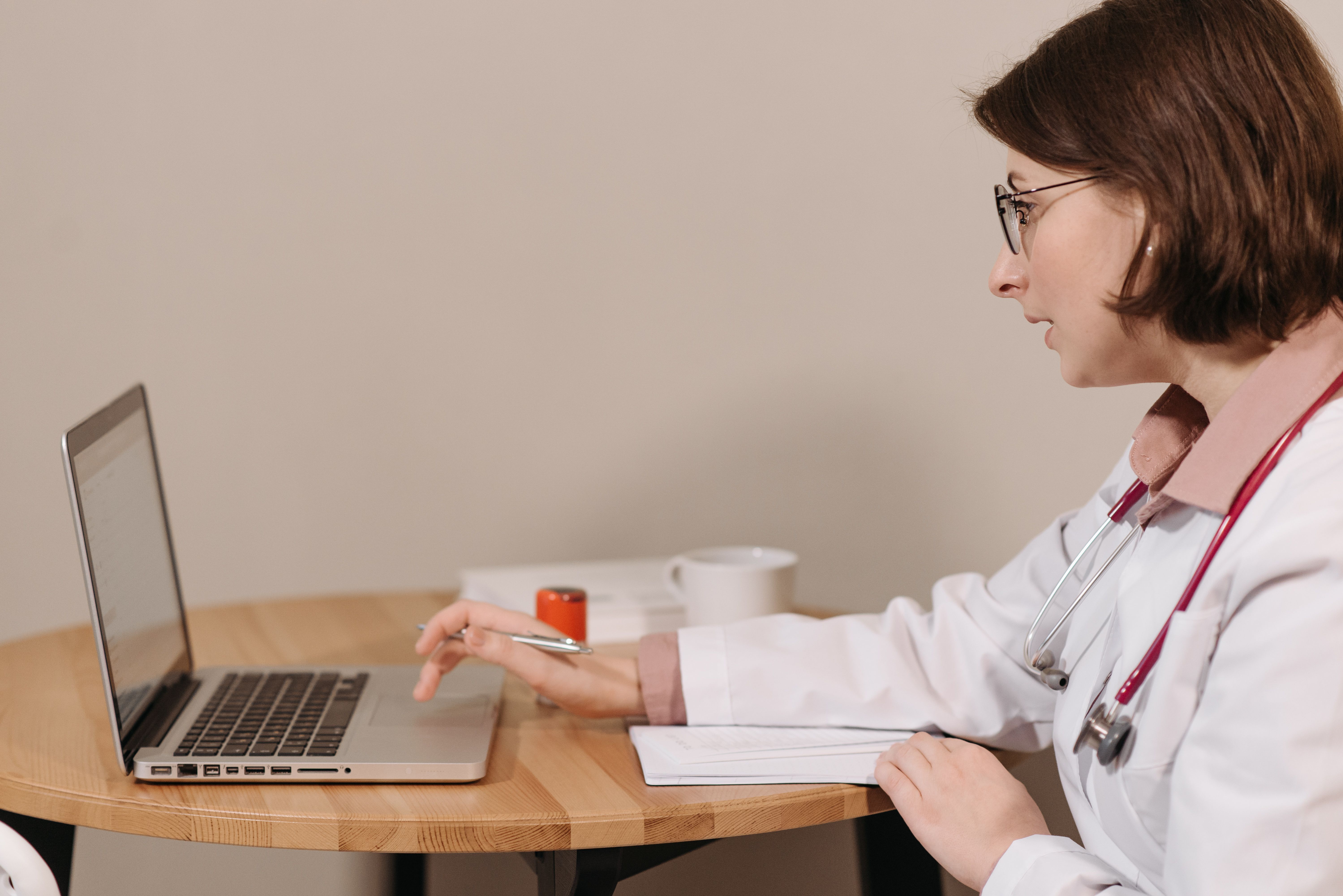 Female doctor using a laptop and writing notes at a clinic workspace